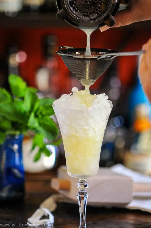 Cocktail being strained into tall cocktail glass filled with crushed ice