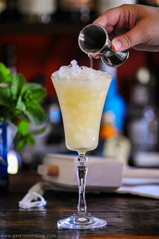 liquid being poured into tall cocktail glass with crushed ice