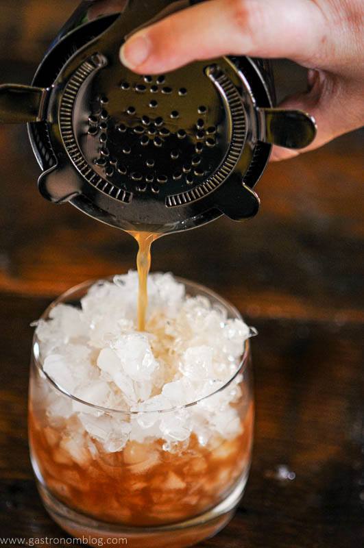 Ancient Mariner cocktail being strianed from cocktail shaker into glass of crushed ice
