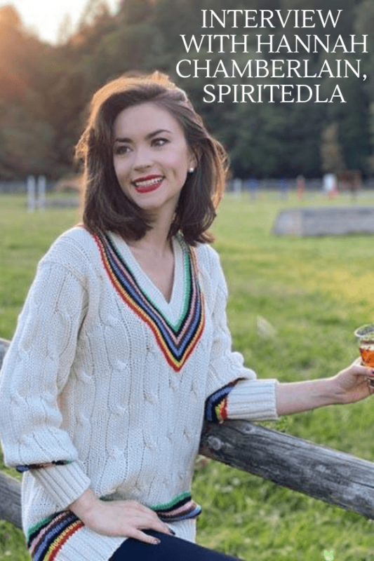 Woman in sweater holding cocktail, standing by a fence