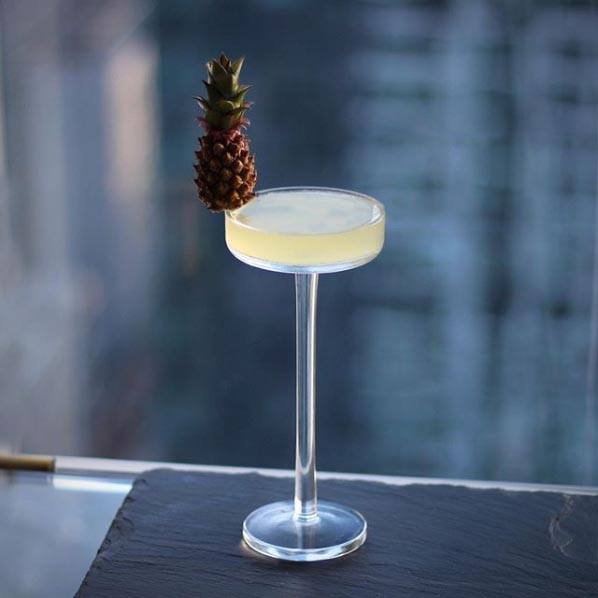 Cocktail in coupe on a ledge, garnished with a tiny pineapple