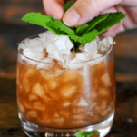Orange cocktail in rocks glass with crushed ice, mint sprig being placed by hand