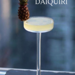 Cocktail in coupe on a ledge, garnished with a tiny pineapple