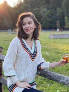 Woman in sweater holding cocktail, standing by a fence