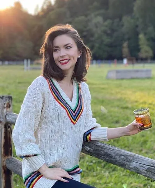 Woman in sweater holding cocktail, standing by a fence