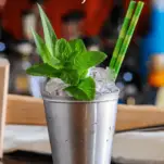 Pineapple Mint Julep in a silver cup with green straws, mint and pineapple fronds
