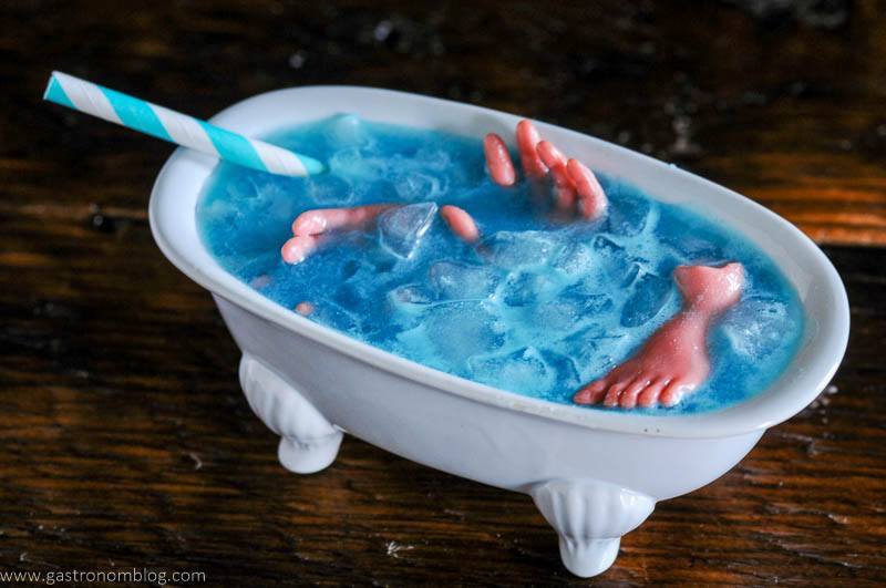Blue cocktail in white bathtub cocktail glass, body parts in cocktail