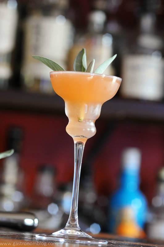 Pink cocktail in tall glass with sage leaves garnish