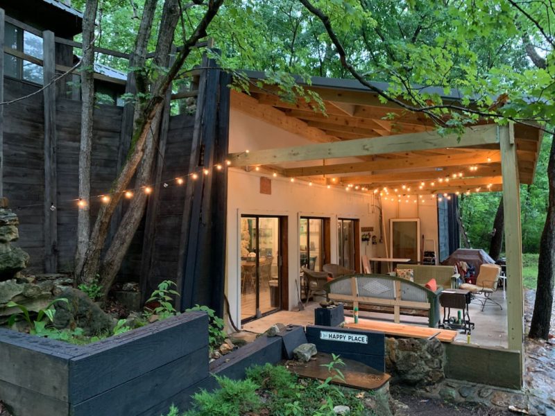 cabin with lights on porch surrounded by trees