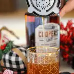 Cocktail being poured from shaker into glass, whiskey bottle behind