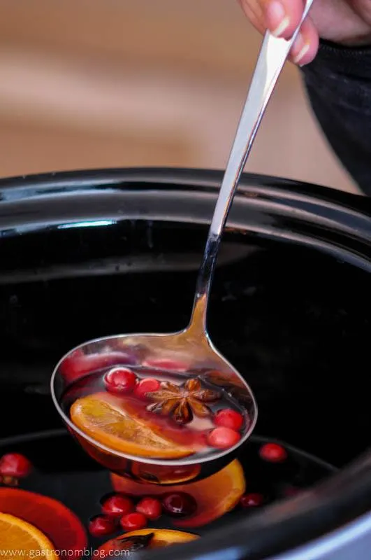 Slow cooker mulled wine with orange slices, cranberries and spices in ladle