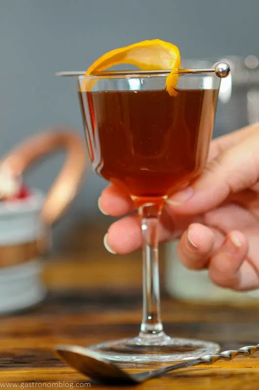 Hand holding cocktail in coupe with orange peel on pick