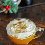 Orange cocktail in tea cup with whipped cream on top, christmas stuff behind
