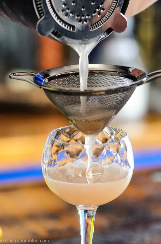 Gin and Jam Cocktail being poured into coupe from shaker with mess strainer