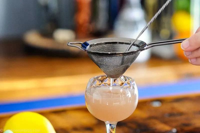 Gin and Jam Cocktail being poured into coupe from shaker with mess strainer