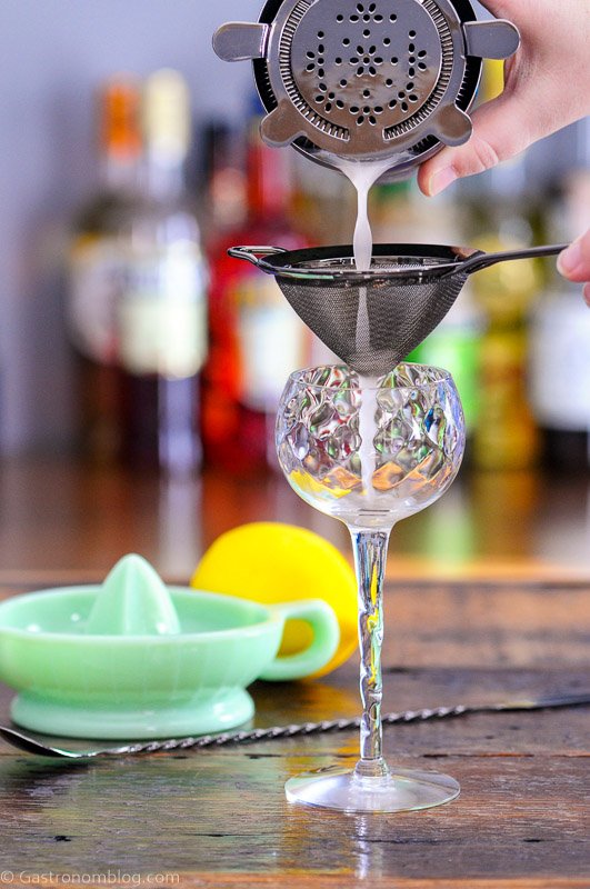 Gin and Jam Cocktail being poured into coupe from shaker with mess strainer