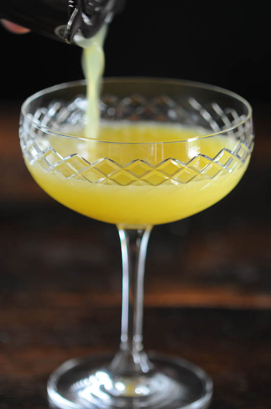 Yellow cocktail being poured into cocktail coupe