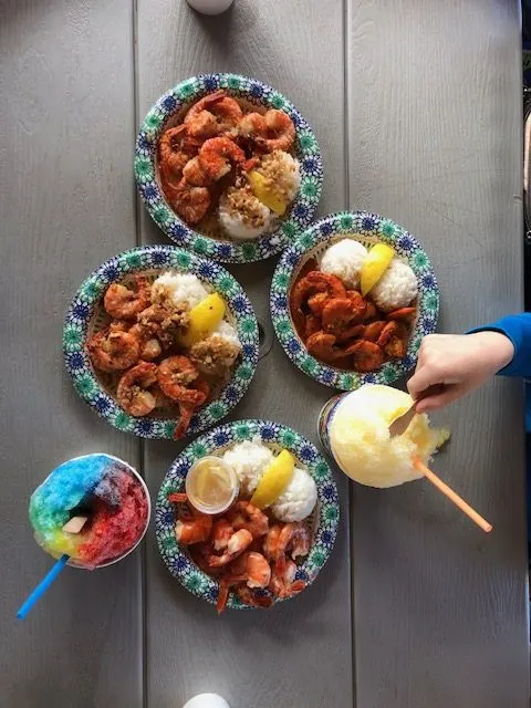 Hand reaching for shave ice and plates of shrimp