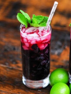 Blueberry Non Alcoholic Mojito, red cocktail in tall glass with mint and silver dotted straw, limes