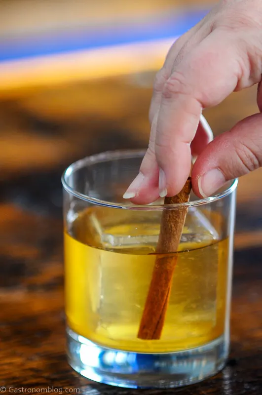 cinnamon stick being placed into a rocks glass with ice