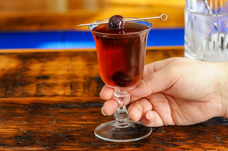 hand holding cocktail in coupe, cherry on pick