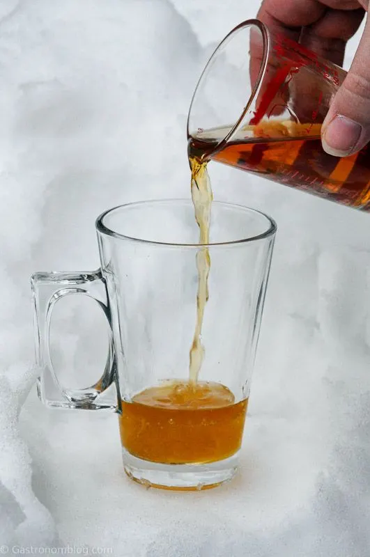 Cognac being poured into glass mug with handle in the snow