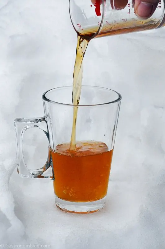 Cognac toddy in glass mug with handle, honey and juice being poured into it