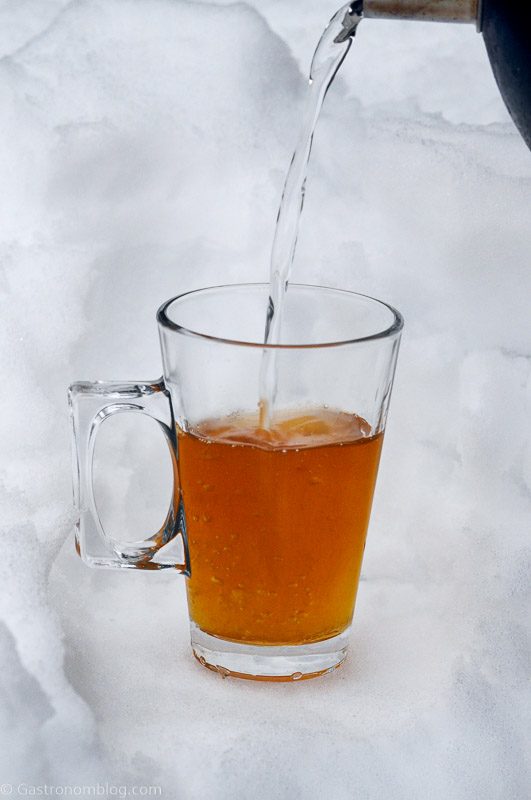 Hot water being poured into glass mug with handle in the snow