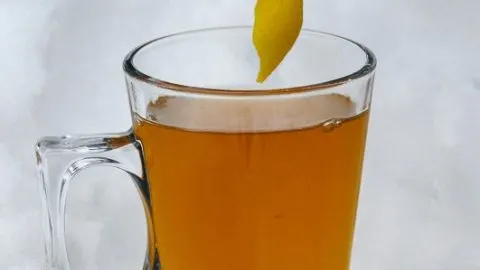 Lemon peel being placed into cognac toddy in glass mug in the snow