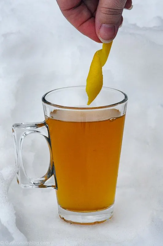 Lemon peel being placed into cognac toddy in glass mug in the snow