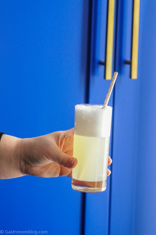 Gin Fizz cocktail recipe in a tall glass with a straw, blue background