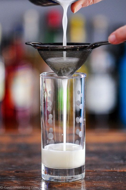 Cocktail being poured into tall glass from shaker through a mesh strainer