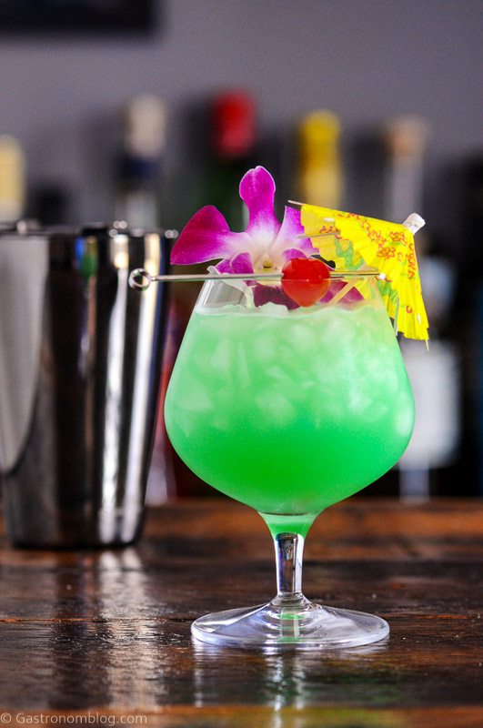 Blue green Blue Hawaii cocktail in balloon glass with crushed ice, paper umbrella, cherry and orchids