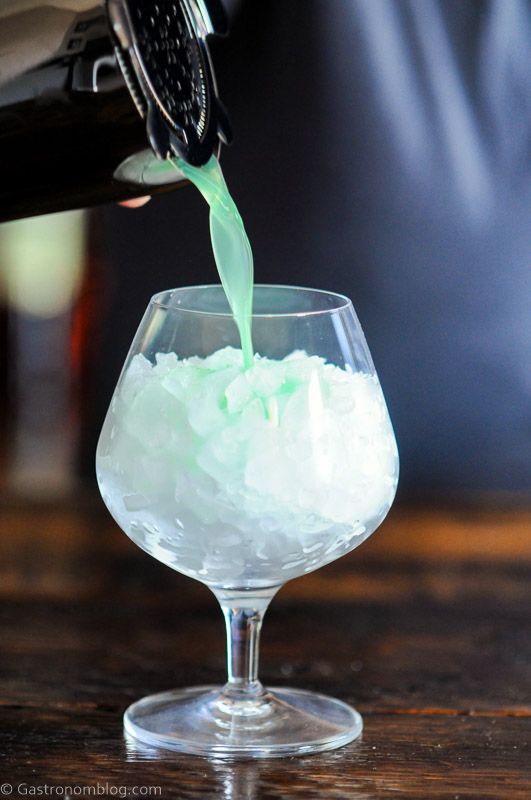 Blue cocktail being poured from shaker in glass with crushed ice