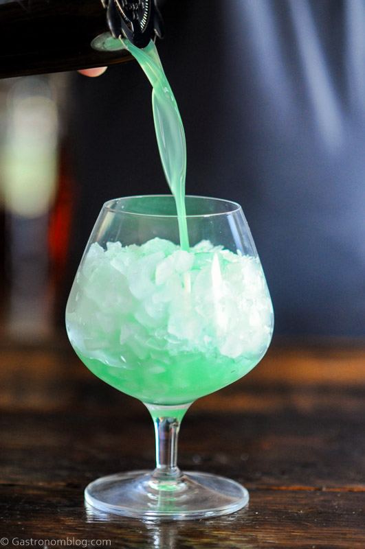 Blue green Blue Hawaii cocktail being poured from shaker in glass with crushed ice