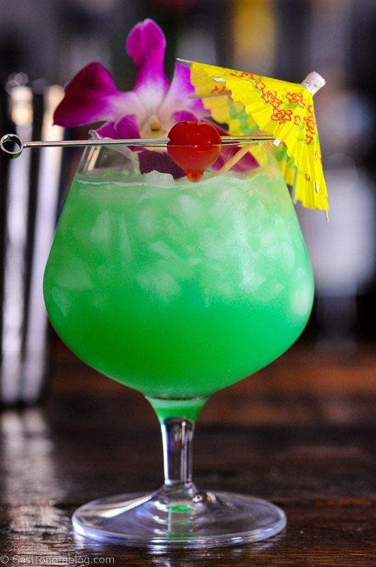Blue green cocktail in balloon glass with crushed ice, paper umbrella, cherry and orchids
