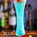 Blue cocktail in a tall glass with flowers and cherry on a pick, orange slice