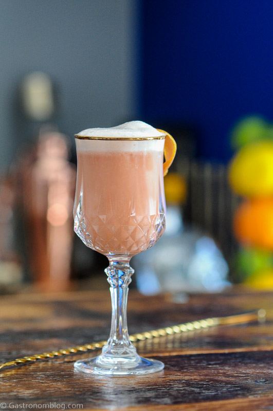 Grapefruit Bourbon Sour, pink cocktail in gold rimmed glass with white foam topping and citrus peel