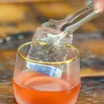 Cranberry cocktail recipe in glass with clear ice in a talon ice tongs