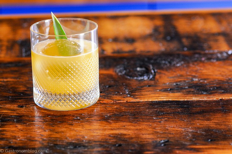 Yellow Tropical Whiskey Cocktail in rocks glass with pineapple frond