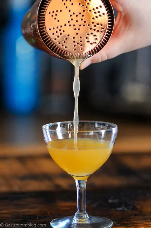 Pouring gold cocktail from bronze shaker