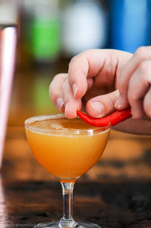 hand placing chili pepper on rim of coupe glass