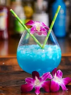 Blue Curacao cocktail being poured into bulb glass, purple and white orchids, bamboo straws