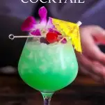 Green cocktail in bulb glass, purple orchid, cherry and yellow umbrella