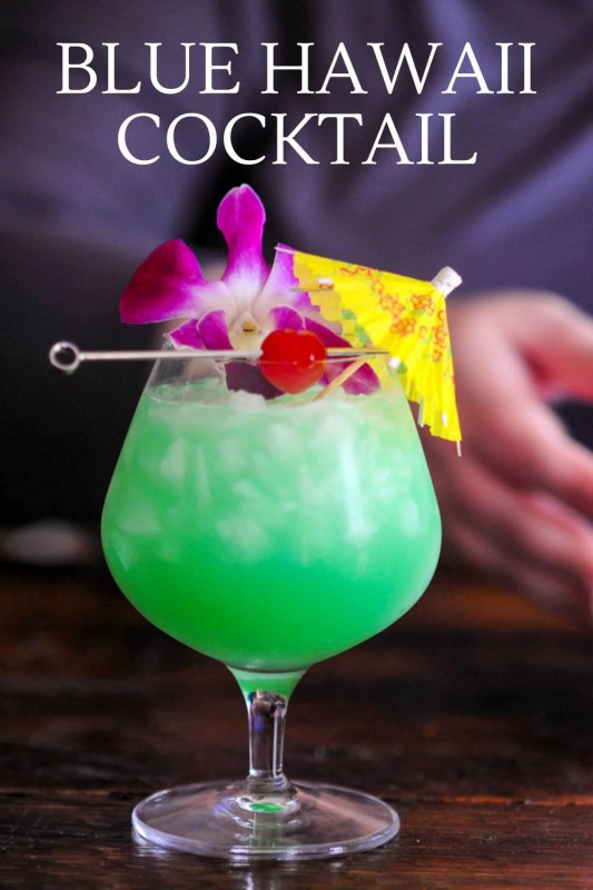 Green cocktail in bulb glass with purple orchid, cherry and yellow umbrella