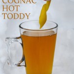Lemon peel being placed into cognac toddy in glass mug in the snow