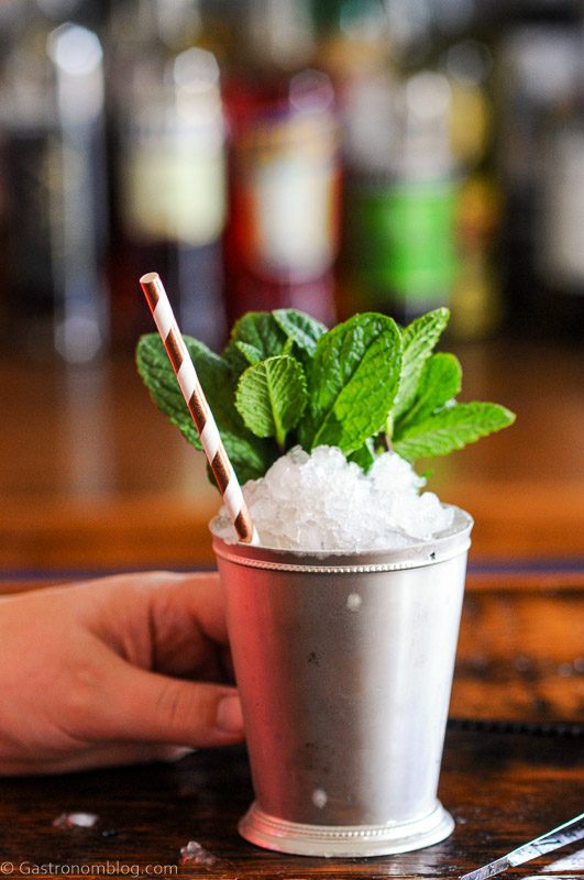hand holding a silver Julep cup with mint sprig and striped paper straw