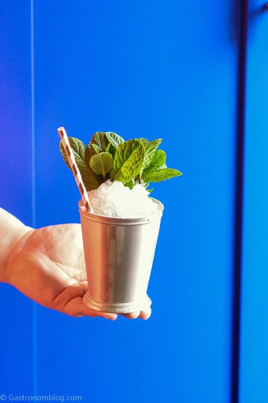 Hand holding silver cup with crushed ice, mint sprig and paper straw