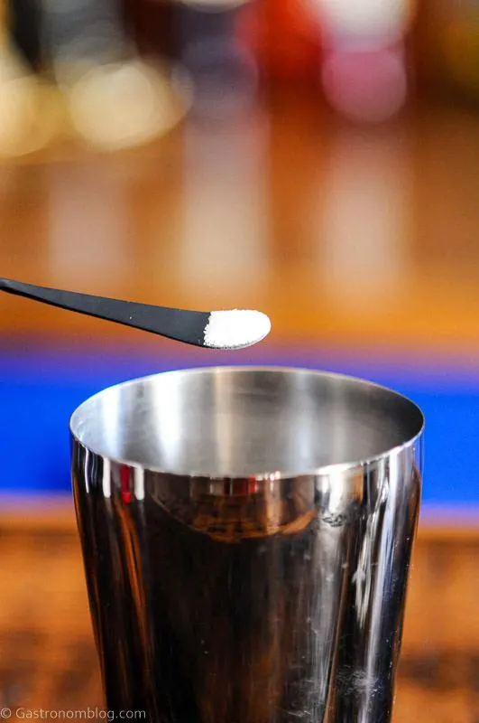 white citric acid powder on bar spoon being poured into a shaker