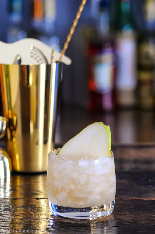 Cocktail in glass with crushed ice, pear slice, gold shaker behind